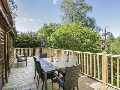 An outdoor wooden deck with a table and chairs next to a log cabin at Striding Edge in White Cross Bay near Troutbeck Bridge