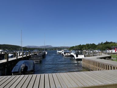 A marina with boats docked between wooden piers and hills in the background at Striding Edge White Cross Bay near Troutbeck Bridge