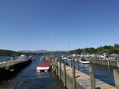 A marina with several boats docked at wooden piers and hills in the background at Striding Edge White Cross Bay near Troutbeck Bridge