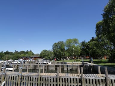 A wooden dock with boats on water and trees in the background at Striding Edge White Cross Bay near Troutbeck Bridge