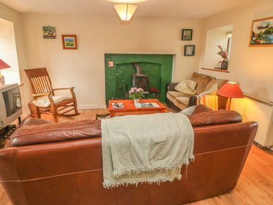 A living room with a brown leather sofa and light green throw blanket facing a green fireplace wooden rocking chair and small sofa with cushions at Nanas House in Allihies County Cork