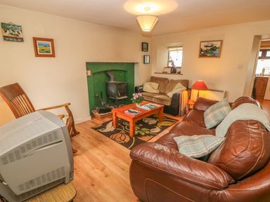 A living room with a wood stove a coffee table two sofas a wooden chair and a television at Nanas House in Allihies County Cork