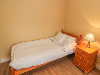 A single bed with white bedding next to a wooden nightstand with a lamp in a bedroom at Nanas House in Allihies County Cork