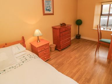A bedroom with a single bed bedside table with lamp chest of drawers wooden chair and window at Nana's House in Allihies County Cork