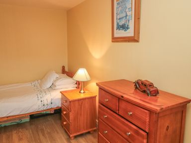 A bedroom with a single bed bedside table lamp wooden chest of drawers and framed picture on the wall at Nanas House in Allihies County Cork