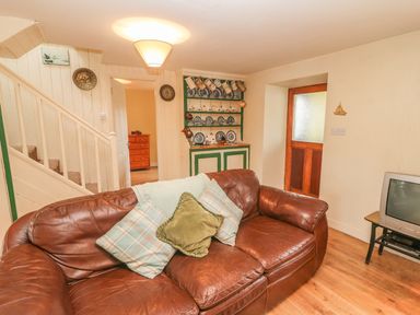 A living room with a brown leather sofa and cushions near stairs and a cabinet with dishes at Nanas House in Allihies County Cork