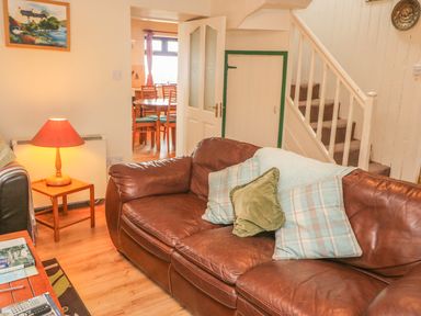 A living room with a brown leather sofa and cushions near stairs and a side table with a lamp at Nanas House in Allihies County Cork