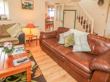 A living room with a brown leather sofa with cushions a wooden coffee table a side table with lamp and a staircase at Nanas House in Allihies County Cork