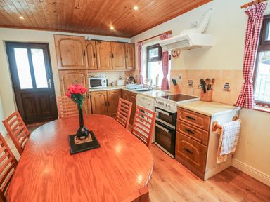 A kitchen with wooden cabinets a dining table with chairs and a vase of flowers at Nanas House in Allihies County Cork