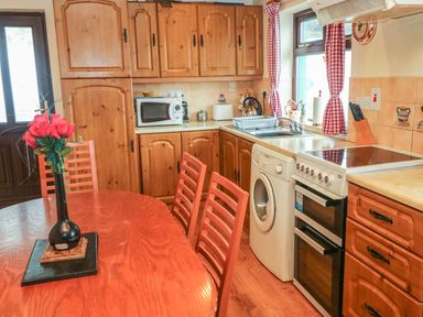 A kitchen with wooden cabinets a dining table with chairs and a vase of flowers at Nana's House in Allihies County Cork