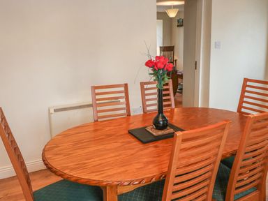 A dining room with a wooden oval table six chairs and a vase with red flowers at Nana's House in Allihies County Cork