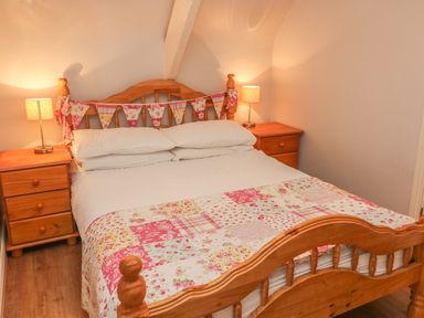 A bedroom with a wooden bed with white pillows and a patchwork quilt flanked by two wooden nightstands with lamps at Nana's House in Allihies County Cork