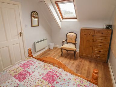 A bedroom with a wooden bed a small wooden cabinet an upholstered chair a wall mirror and a skylight window at Nana's House in Allihies County Cork
