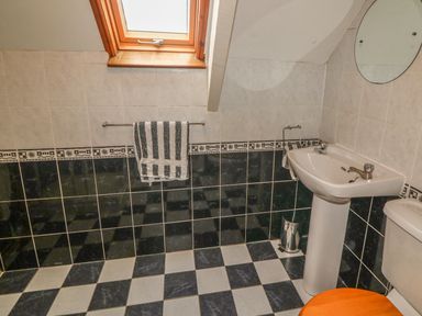 A bathroom with checkered floor tiles a towel on a rail a pedestal sink mirror and toilet at Nanas House in Allihies County Cork