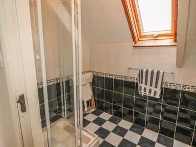 A bathroom with a glass shower enclosure a striped towel hanging on a wall rack and a wooden towel stand by a small window at Nanas House in Allihies County Cork