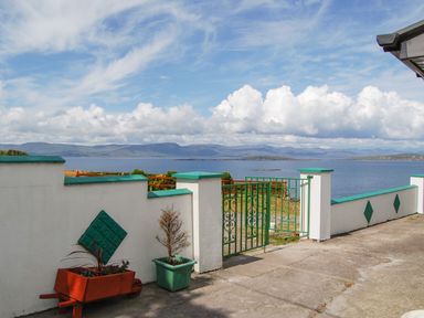 An outdoor area with a white wall and green gate overlooking a body of water and distant hills at Nana's House in Allihies County Cork