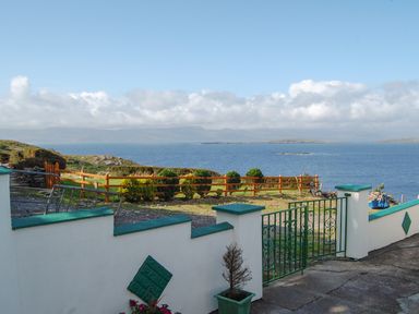 A garden with a white wall and green metal gate overlooking the sea and distant mountains at Nanas House in Allihies County Cork