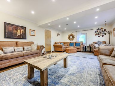 A living room with brown sofas a wooden coffee table blue patterned rugs and wall art at Eden House in Bardsea