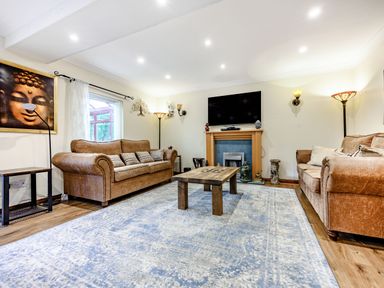 A living room with two brown sofas a wooden coffee table a television above a fireplace and a large blue patterned rug at Eden House in Bardsea