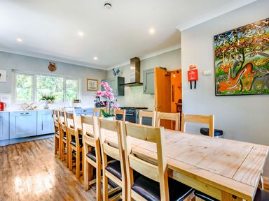 A kitchen with a long wooden dining table and chairs a stove cabinets and a painting on the wall at Eden House in Bardsea