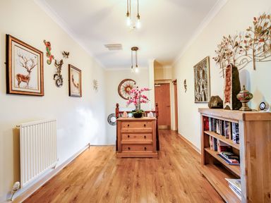 A hallway with wooden flooring and furniture including a chest of drawers and a bookshelf with books at Eden House in Bardsea