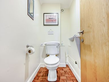 A small bathroom with a white toilet a wall-mounted sink a wooden door and framed pictures on the wall at Eden House in Bardsea