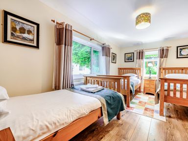 A bedroom with three single wooden beds a nightstand a table lamp curtains and framed pictures on walls at Eden House in Bardsea