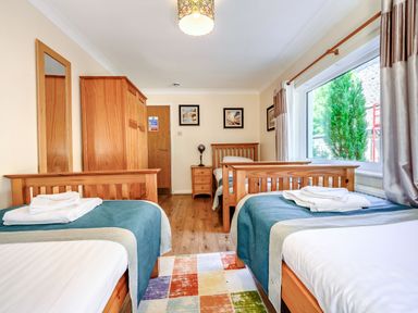 A bedroom with two single beds wooden furniture and a large window at Eden House in Bardsea
