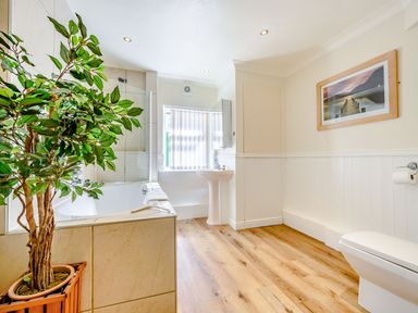 A bathroom with a bathtub a sink a toilet a potted plant and a framed picture on the wall at Eden House in Bardsea