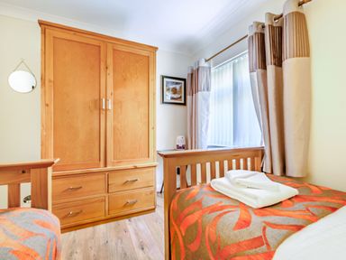 A bedroom with a wooden wardrobe beds with patterned bedspreads and curtains at Eden House in Bardsea