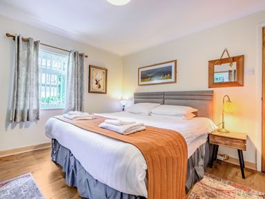 A bedroom with a large bed bedside tables lamps framed pictures and a window with curtains at Eden House in Bardsea