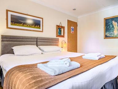A bedroom with a large bed white pillows folded towels and framed pictures on the walls at Eden House in Bardsea