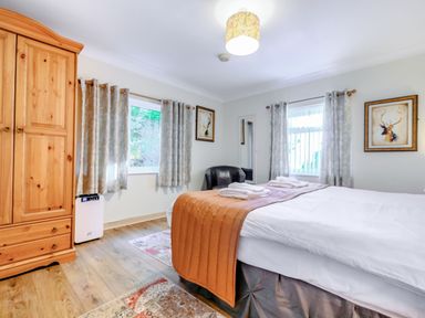 A bedroom with a bed covered with folded towels a wooden wardrobe a black armchair two windows with curtains and two paintings on the walls at Eden House in Bardsea