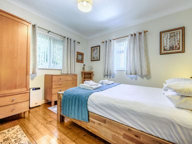 A bedroom with a wooden bed and dresser and two windows with curtains at Eden House in Bardsea