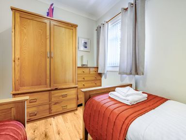 A bedroom with a wooden wardrobe a chest of drawers two single beds with orange bed covers and a window with gray curtains at Eden House in Bardsea