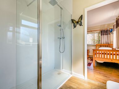 A bathroom with a glass shower enclosure and a wooden bed visible in the adjacent bedroom at Eden House in Bardsea