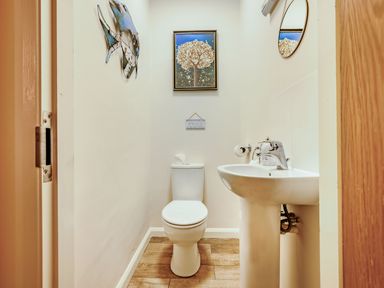 A small bathroom with a white toilet and pedestal sink a mirror and artwork on the walls at Eden House in Bardsea