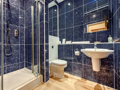 A bathroom with a shower cubicle toilet and sink with blue tiled walls and wooden floor at Eden House in Bardsea