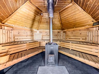 A wooden sauna room with benches along the walls and a heating stove in the center at Eden House in Bardsea