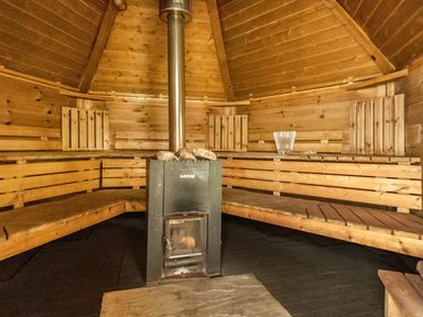An interior of a wooden sauna with benches along the walls and a central stove with stones at Eden House in Bardsea