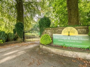A gated entrance with trees and stone walls showing a sign for Eden Lodge and Eden House in Bardsea