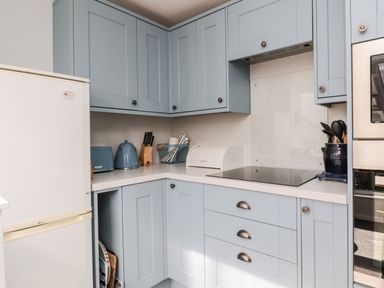 A kitchen corner with blue cabinets white countertop a white refrigerator a toaster kettle and knife block at Lyndhurst Cottage in Beadnell