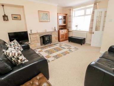 A living room with two black leather sofas a rug a wooden cabinet and a fireplace at Lyndhurst Cottage in Beadnell