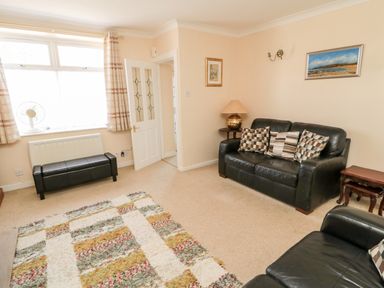 A living room with black leather sofas pillows a floor lamp a patterned rug and a window with curtains at Lyndhurst Cottage in Beadnell