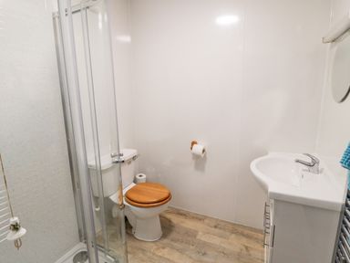 A bathroom with a shower enclosure toilet with wood seat and white sink at Lyndhurst Cottage in Beadnell