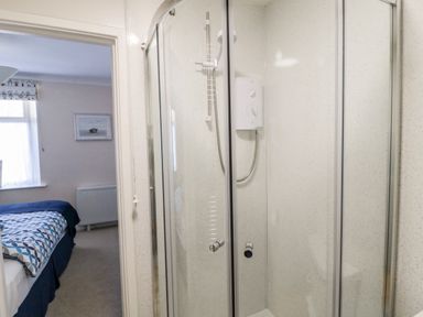 A bathroom with a corner shower unit and a bedroom visible through an open door at Lyndhurst Cottage in Beadnell