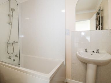A bathroom with a bathtub shower combination and a pedestal sink at Lyndhurst Cottage in Beadnell