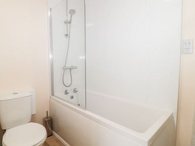 A bathroom with a toilet next to a bathtub with a shower at Lyndhurst Cottage in Beadnell