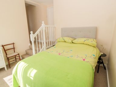 A bedroom with a bed with green bedding stairs with white railing a wooden chair and a nightstand at Lyndhurst Cottage in Beadnell
