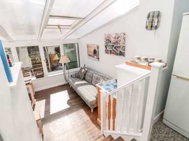A sunroom with a plaid sofa floor lamp and two paintings above the sofa at Lyndhurst Cottage in Beadnell